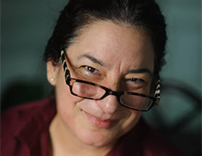 Close-up of a person wearing glasses and a maroon shirt smiling slightly.
