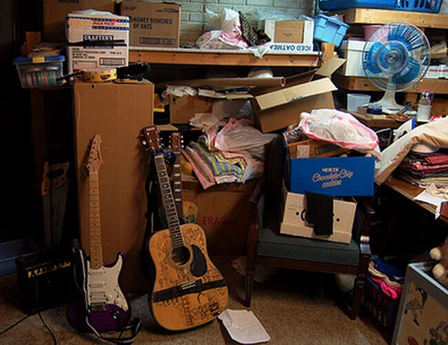 Messy room filled with cardboard boxes, miscellaneous items, and two guitars.