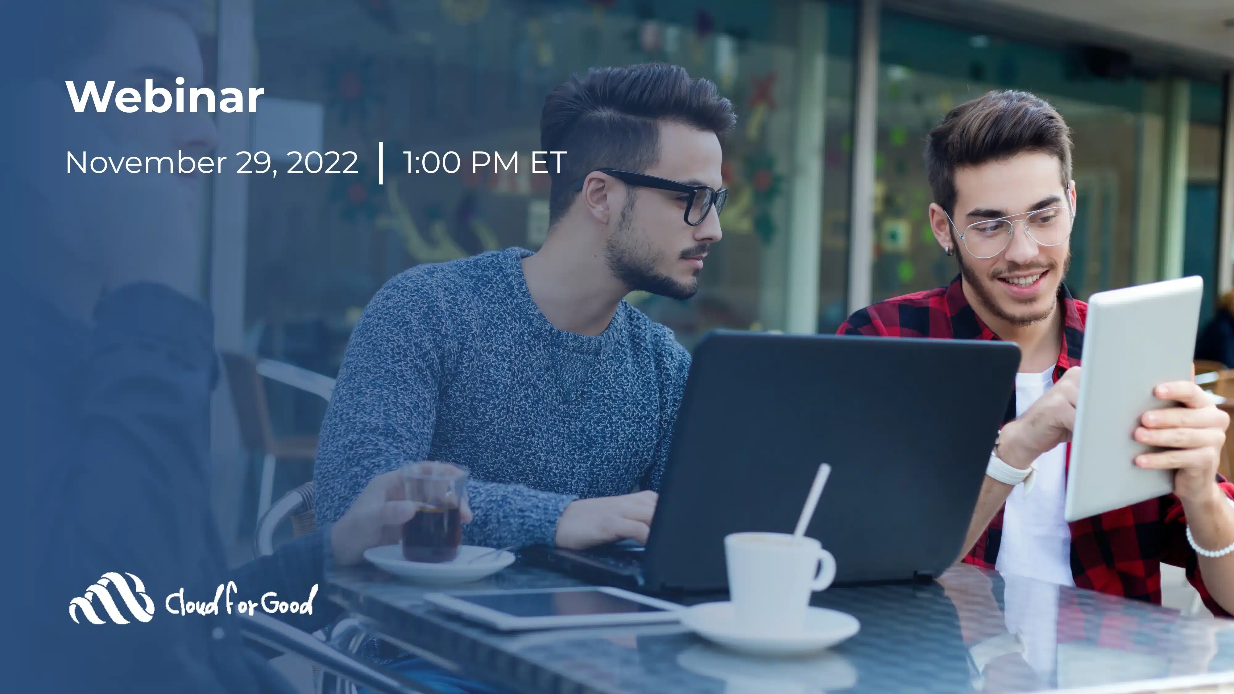 Two young men at an outdoor café table with a laptop, tablet, and coffee