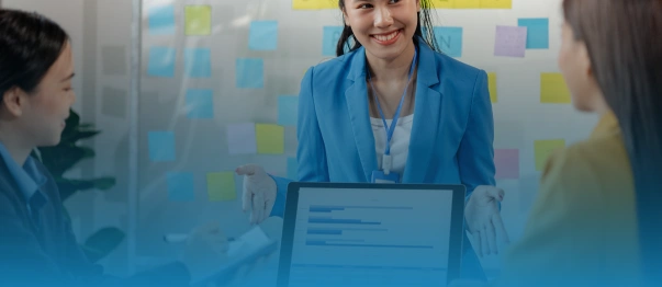Three coworkers discussing a laptop with a bar chart in front of a wall of sticky notes