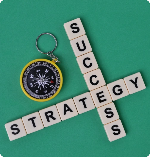 Letter tiles spelling strategy and success beside a compass on a green surface