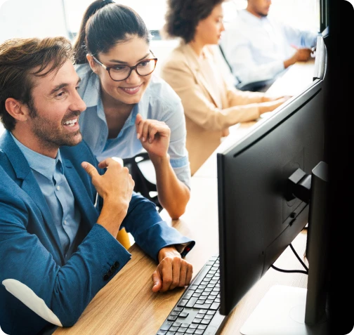 Two coworkers smiling while working at desktop computers in a bright office