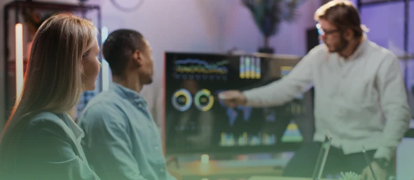 Presenter explaining an analytics dashboard to two coworkers in a meeting room