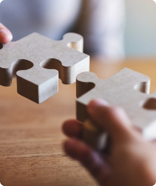 Hands holding two puzzle pieces close together on a wooden table