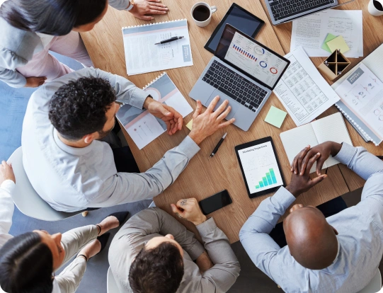 Overhead view of a team reviewing reports, laptops, and tablets around a meeting table