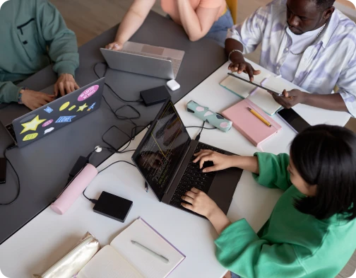 Overhead view of a team working at a table with laptops, notebooks, and a tablet