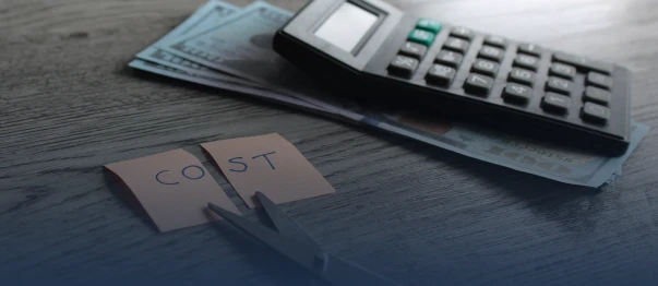 Calculator and cash on a table with torn paper spelling the word cost