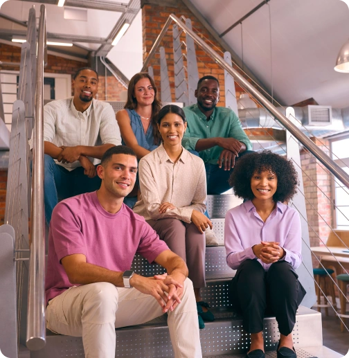 Six coworkers sitting together on office stairs and looking at the camera