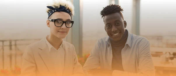 Two coworkers sitting together at a table and looking toward the camera